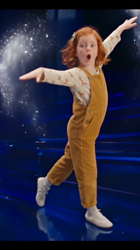 Red-haired child dancing with outstretched arms on a dark blue stage with bright sparkles
