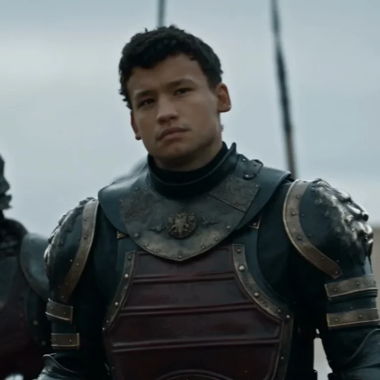 A dark-haired person in dark metal armor facing the camera against a pale sky