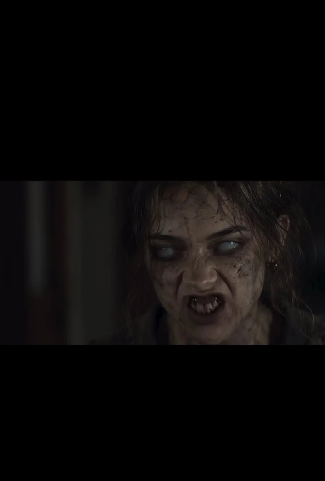 Close-up of a woman with pale eyes and an infected appearance in a dark scene