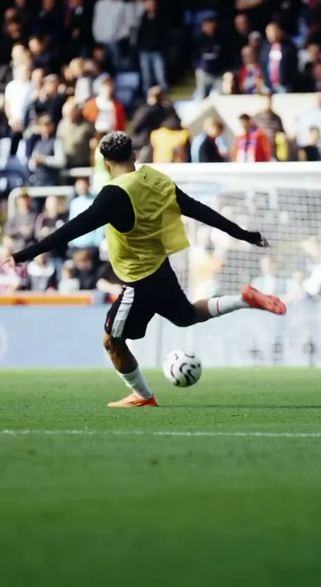 Football player in a yellow training bib striking a ball in front of a goal