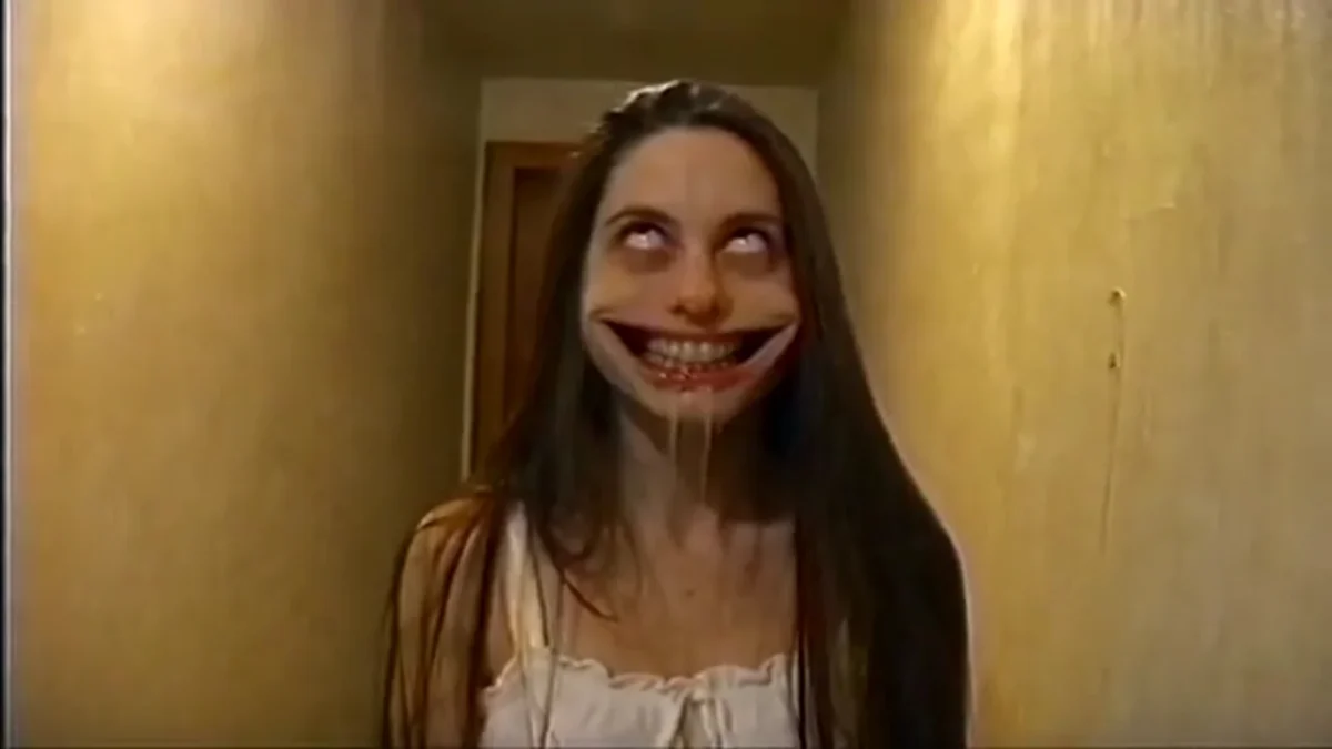 Source preview of a long-haired person in a white nightgown with rolled-back eyes and a stretched grin in a narrow yellow hallway