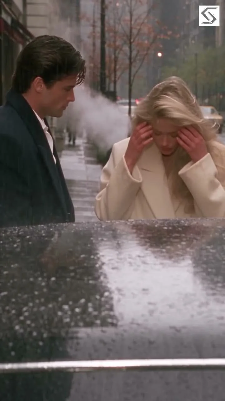 A man and blonde woman meet beside a rain-speckled car on a wet city street