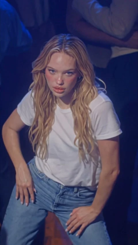 Blonde woman in a white T-shirt and jeans dancing under blue light in a crowded club